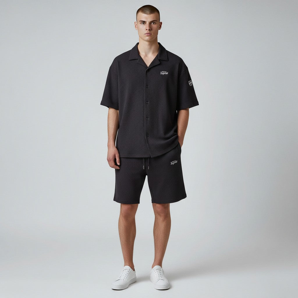 Klothco Kaporal black textured short-sleeve button-down shirt and matching drawstring shorts set on a male model.