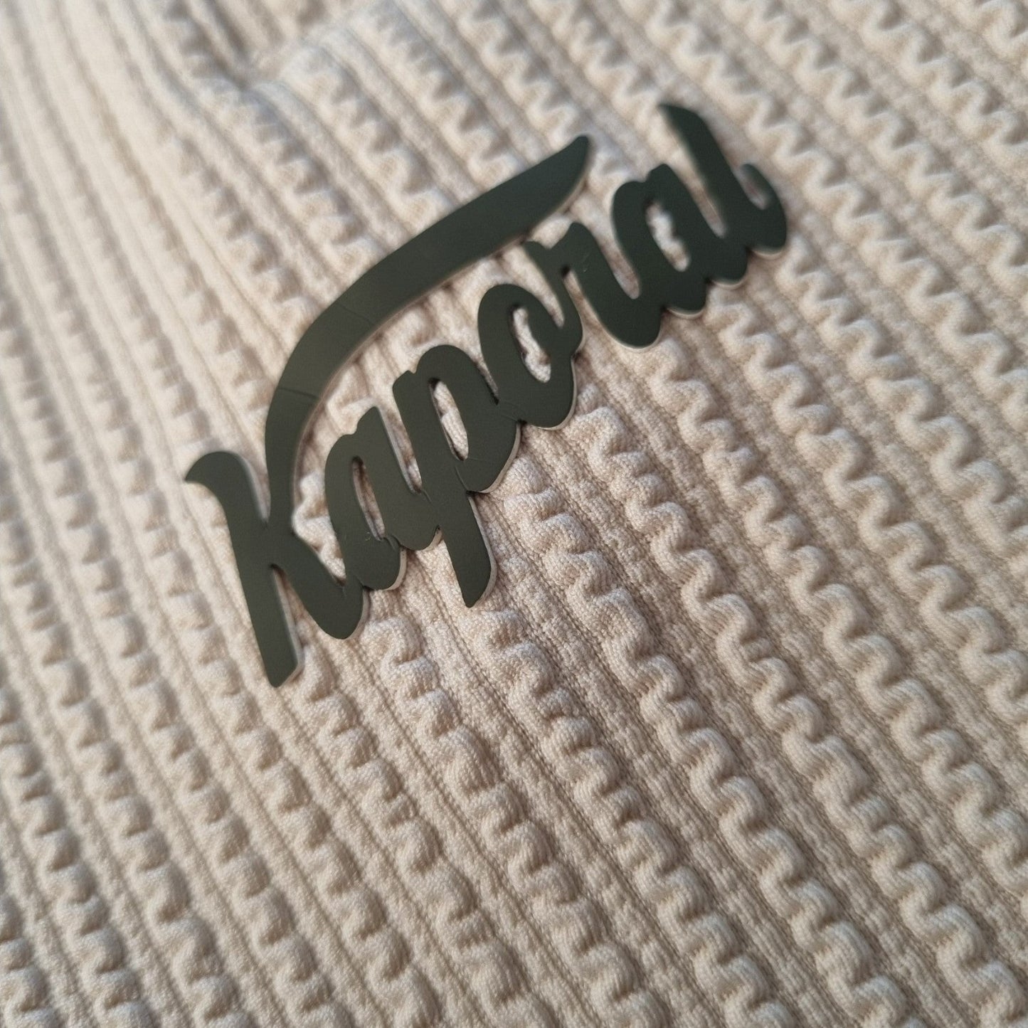 Klothco Kaporal beige textured fabric with a black script logo patch detail