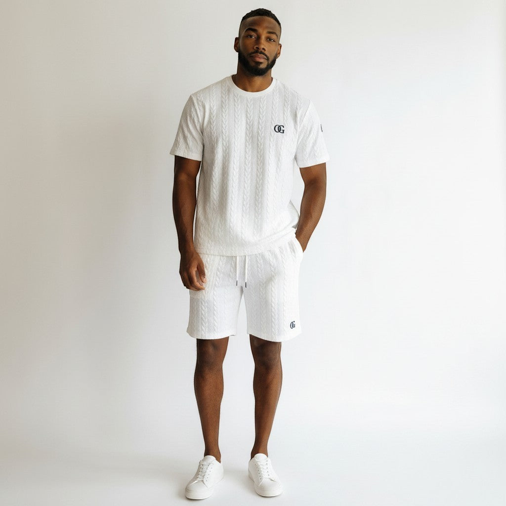 A man wearing a white Klothco cable-knit short sleeve shirt and matching shorts set with a drawstring waist.